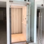 Symmetry Home Elevator with painted white interior and glass door with stainless steel handle. Installed by Area Access