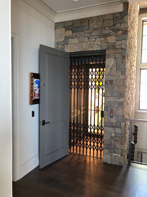 Custom home elevator with accordion gate, stone, and painting