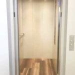 Symmetry LULA Elevator in standard steel panels painted Ivory with standard Bushed Stainless Steel car operating panel (COP) and handrail, floor by others