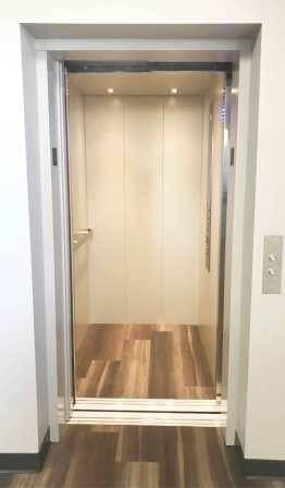 Symmetry LULA Elevator in standard steel panels painted Ivory with standard Bushed Stainless Steel car operating panel (COP) and handrail, floor by others